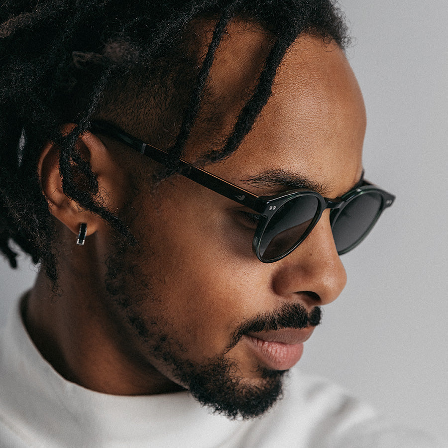 Black man wearing olive green sunglasses looking down