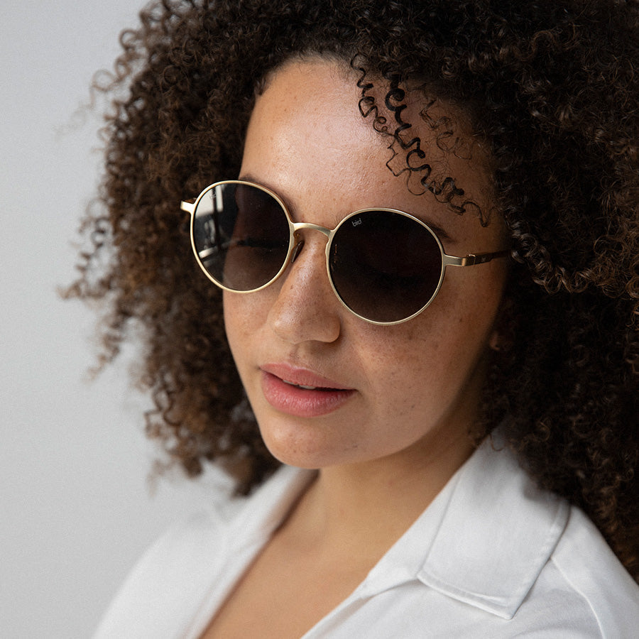 Black woman wearing round sunglasses with gold frame and grey lenses